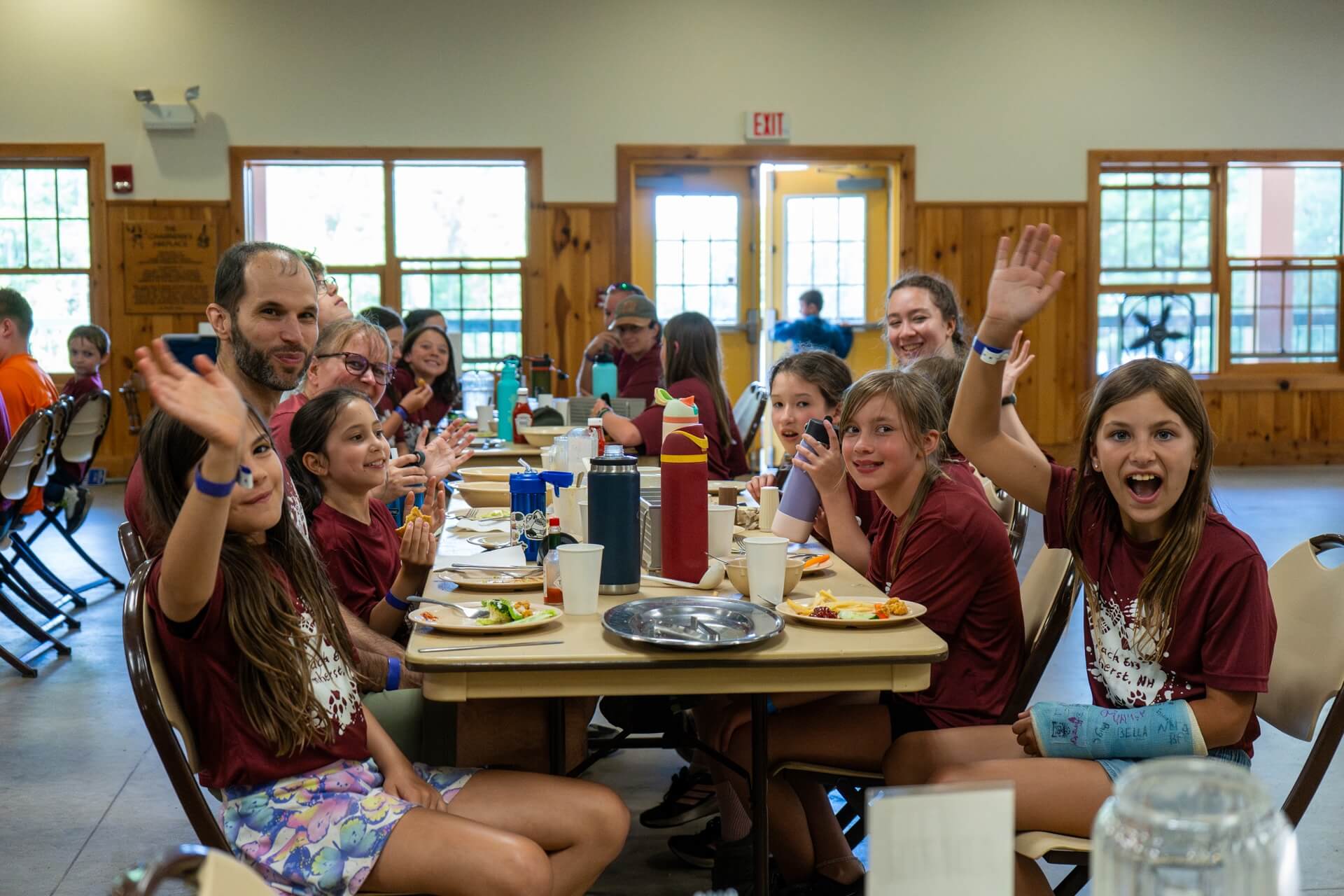 Scouts enjoying a meal together at Camp Carpenter summer camp, smiling and waving inside the camp dining hall.